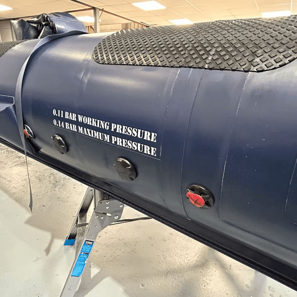 Close-up of a blue military RIB tube showing 0.11 bar working pressure and 0.14 bar maximum pressure markings